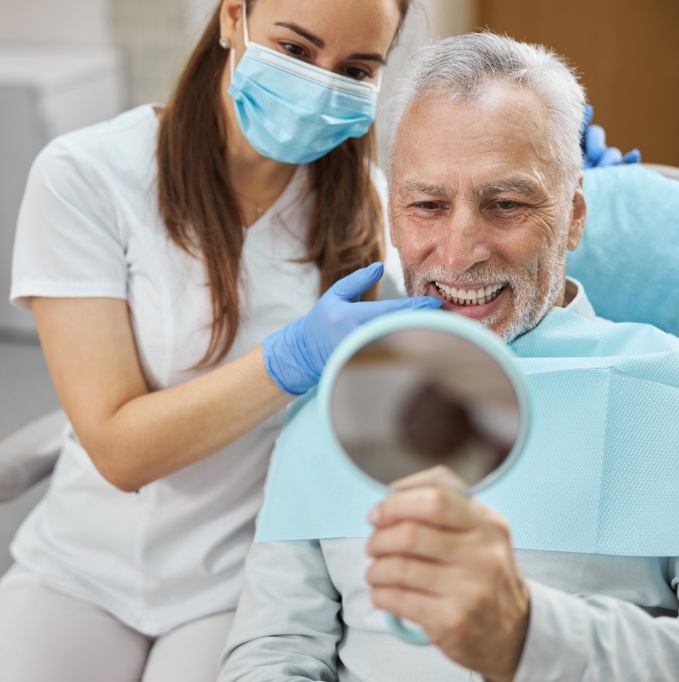 Male dental patient smiling at handheld mirror with dentist next to him