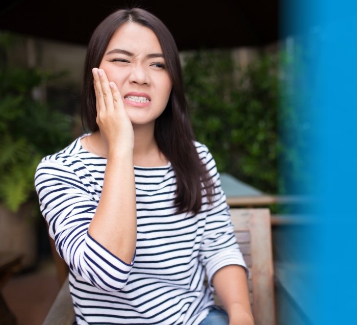 Woman in striped shirt with tooth pain in need of emergency dentist in San Jose