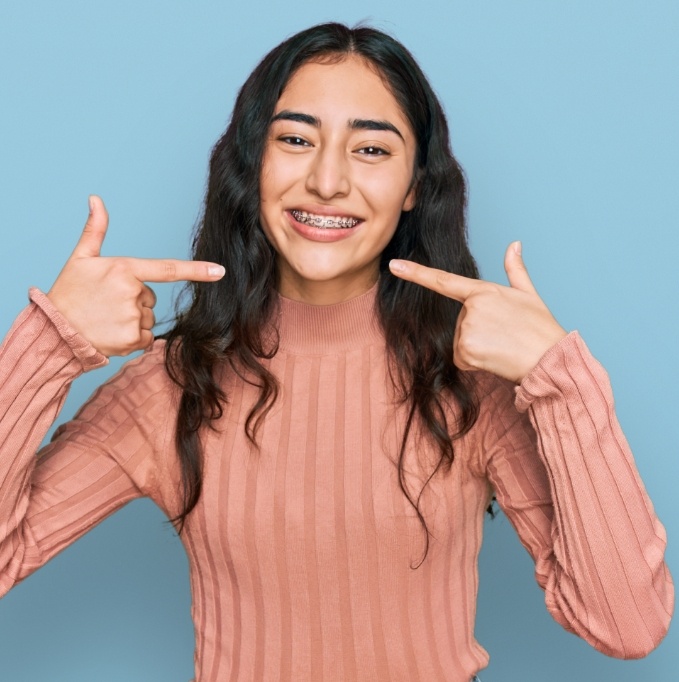 Woman in sweater pointing to braces and smiling