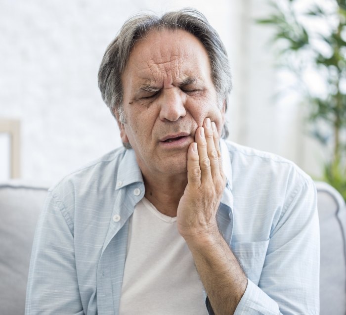 Man sitting on couch with jaw pain needing TMJ treatment in San Jose